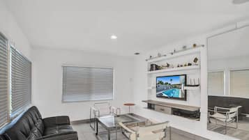 Un salon moderne avec un canapé, une table basse en verre, un téléviseur fixé au mur et une bibliothèque agrémentée d’objets décoratifs.
