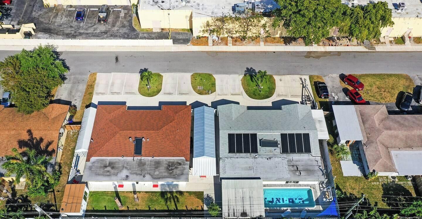An aerial view of a building with a flat roof, a swimming pool, and a parking lot.
