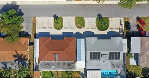 An aerial view of a parking lot with multiple cars, a building with a red roof, and green landscaped areas. - Private unit w/pool view & patio (Deerfield Beach)