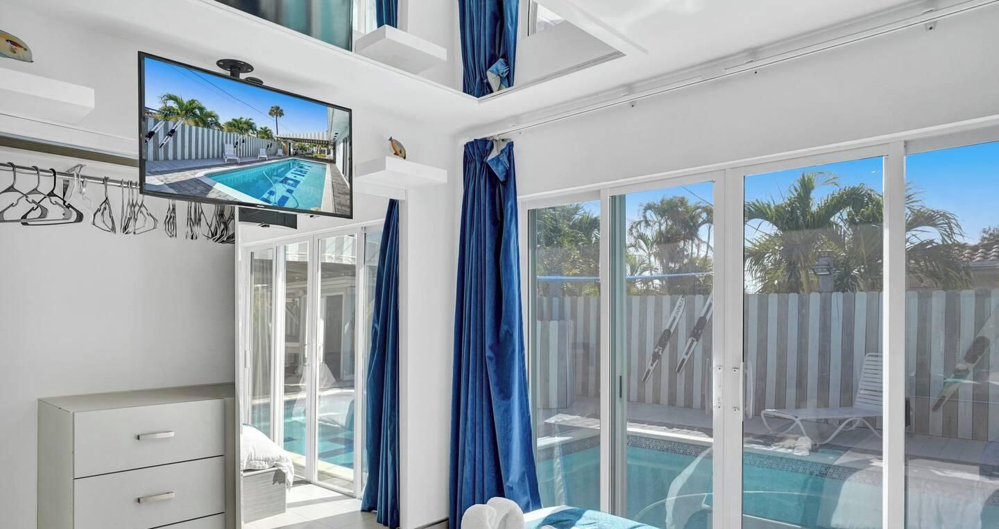 Une chambre dotée d’une grande fenêtre, d’un téléviseur à écran plat et d’une piscine visible à travers les portes vitrées.