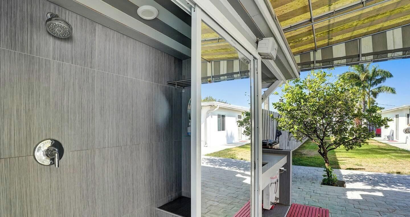 Un baño moderno con ducha, toallero y puerta de vidrio que da a un espacio exterior con un árbol y un camino.