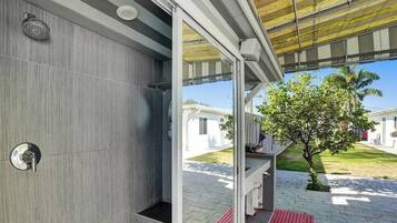 Un baño moderno con ducha, toallero y puerta de vidrio que da a un espacio exterior con un árbol y un camino.
