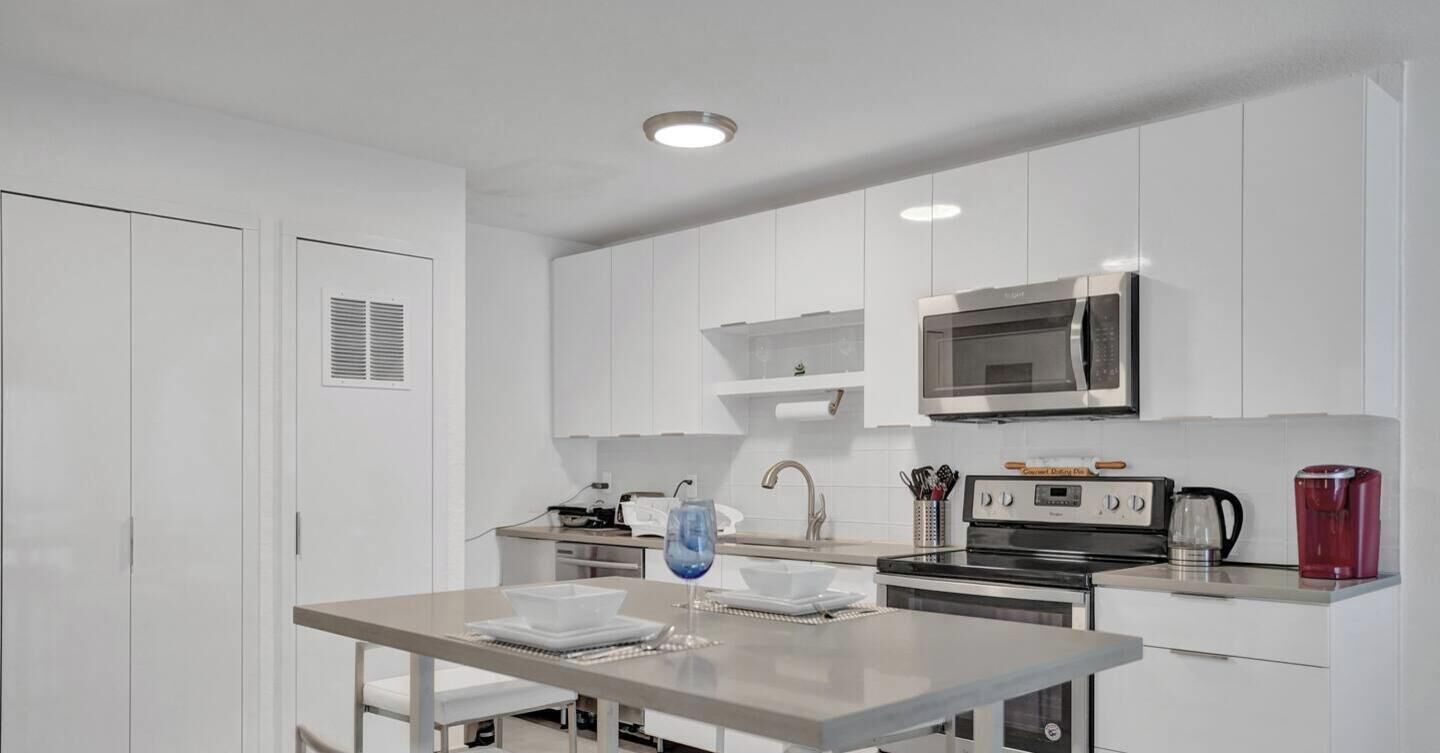Een moderne keuken met witte kasten, een roestvrijstalen magnetron, een oven en een koffiezetapparaat.
