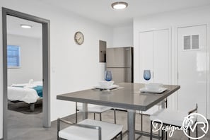 A modern room with a bed, a dining table with chairs, a clock on the wall, and a refrigerator. - Private house w/pool & patio (Deerfield Beach)