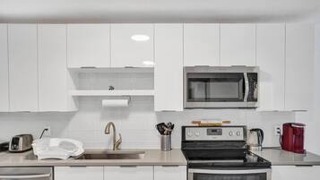 Una cocina moderna con gabinetes blancos, un lavamanos de acero inoxidable, un microondas, una estufa a gas y una cafetera roja.