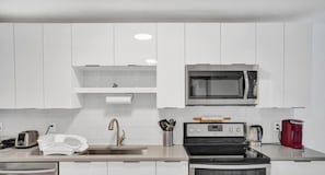 A modern kitchen with white cabinets, a stainless steel sink, a microwave, a gas stove, and a red coffee maker. - Private house w/pool & patio (Deerfield Beach)