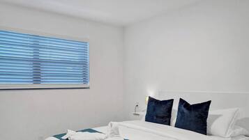 Una habitación de hotel con una cama, un ventanal con persianas y una mesita de noche con lámpara.