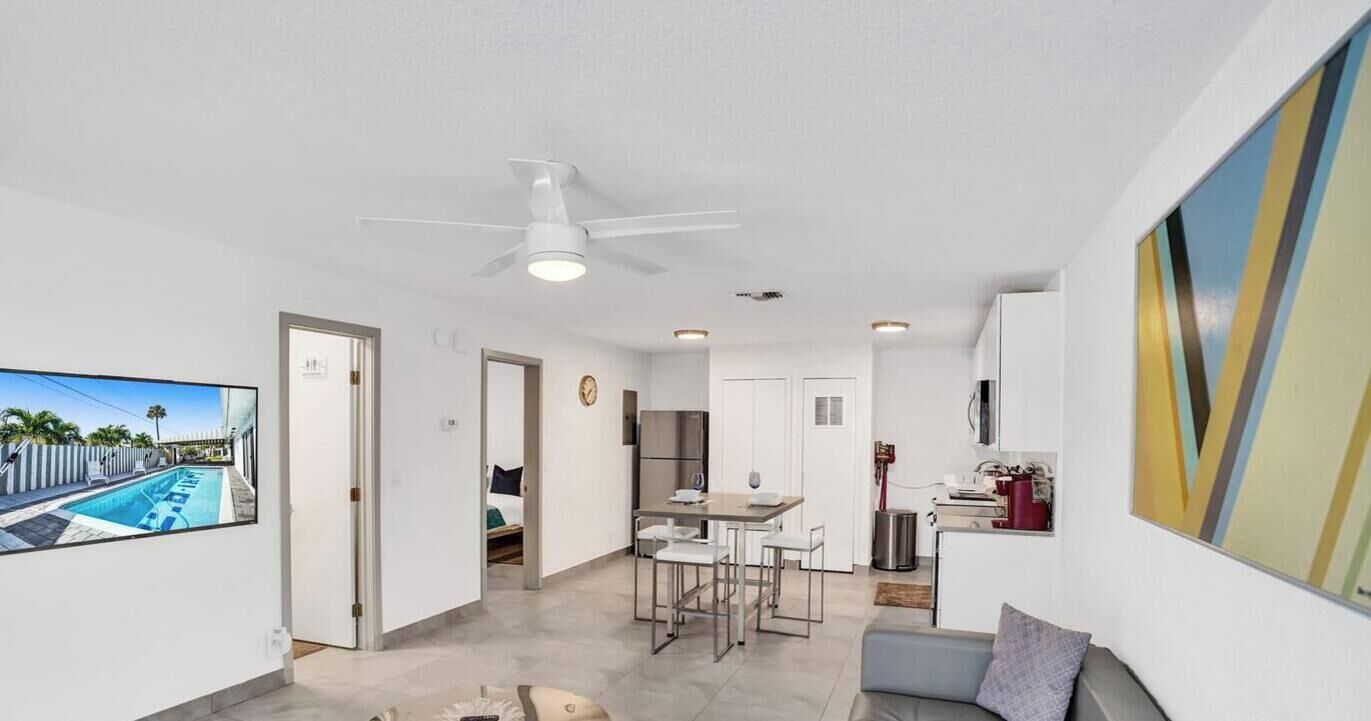 Un soggiorno moderno con una TV a schermo piatto, un ventilatore a soffitto e un'area pranzo con cucina sullo sfondo.