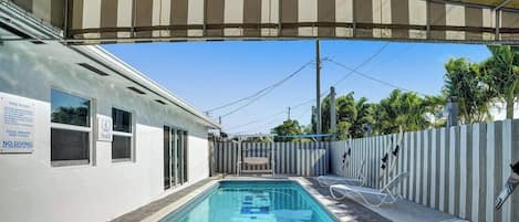 Piscina com área coberta, cadeira de salva-vidas e placa com regras da piscina.