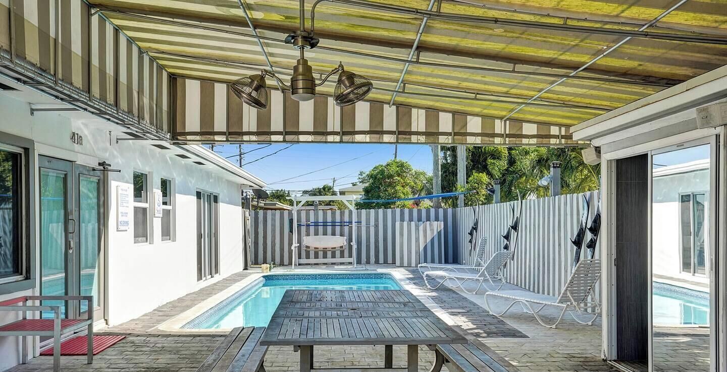 A covered outdoor swimming pool area with a table and lounge chairs.
