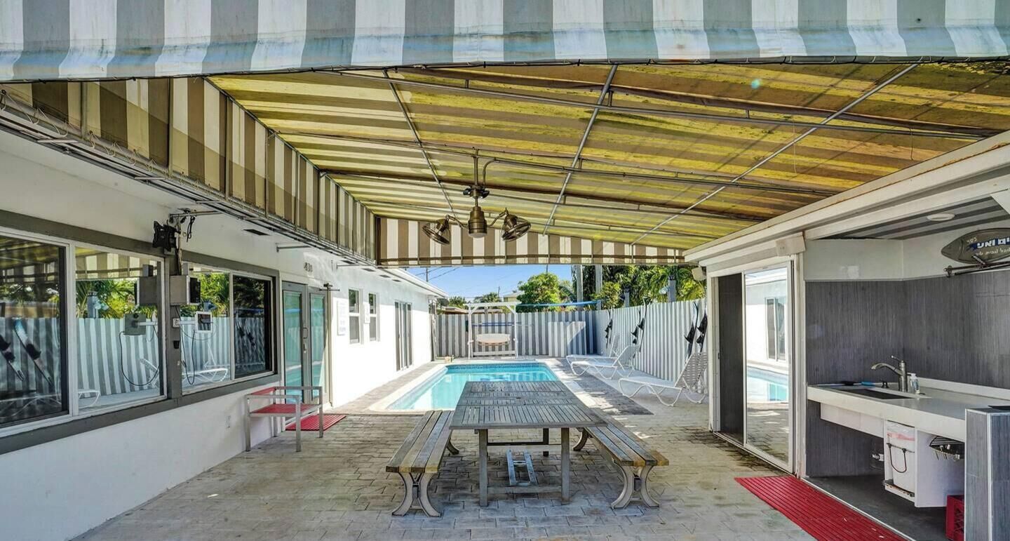 A covered outdoor area with a pool, a table, and a kitchen area.