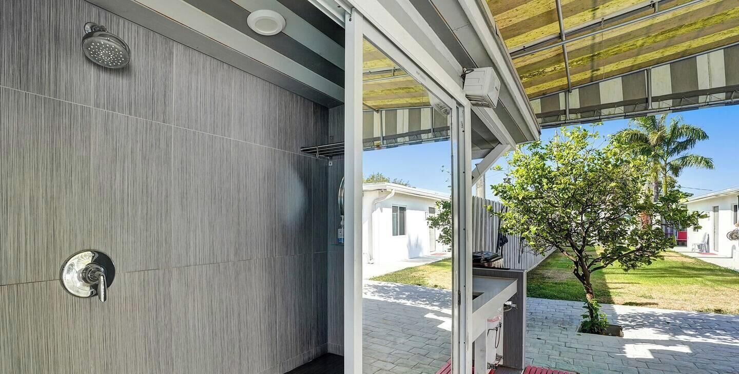 A modern bathroom with a shower, a towel rack, and a glass door leading to an outdoor area with a tree and a pathway.