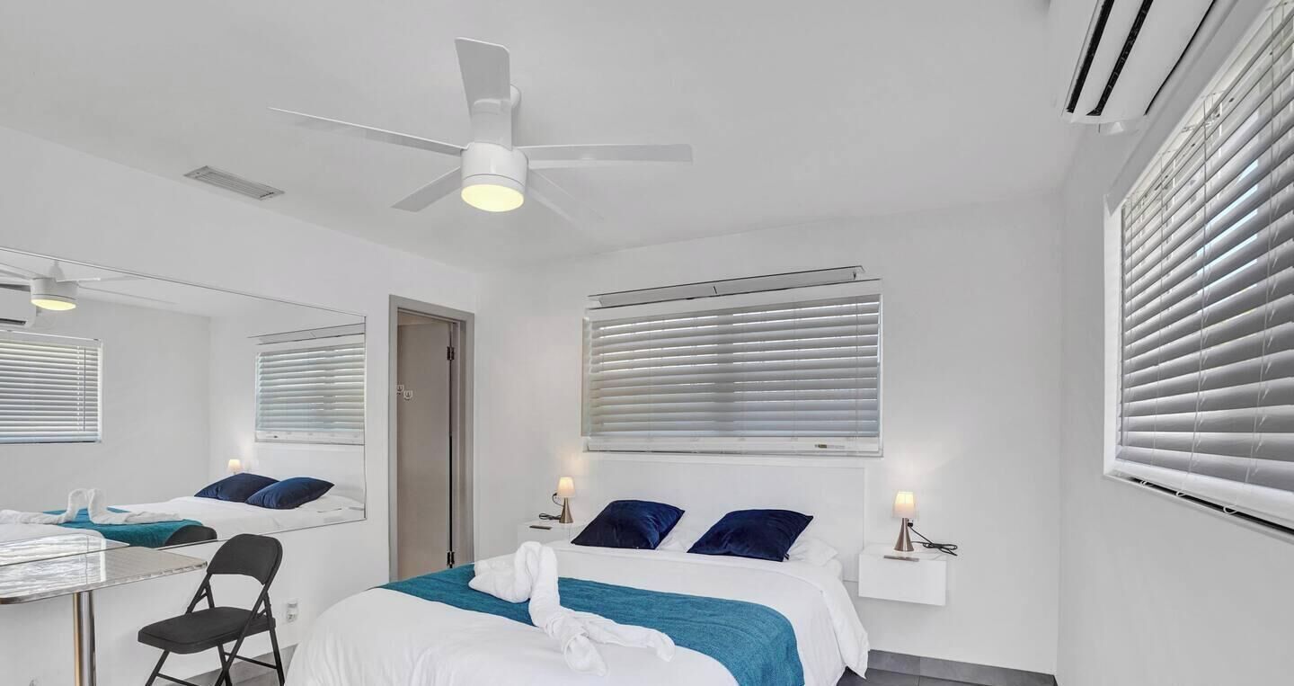 Een hotelkamer met een bed, een bureau, een stoel, een plafondventilator en een raam met zonwering.