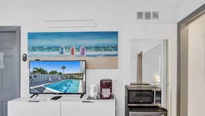 Une chambre dotée d’un téléviseur à écran plat diffusant une vue sur la piscine, d’une machine à café, d’un four à micro-ondes et d’un tableau représentant des planches de surf accroché au mur.