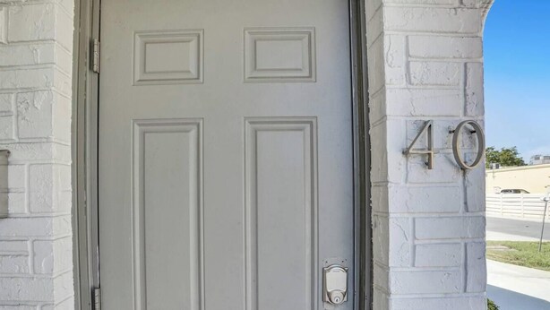 Une porte blanche ornée d’un panneau rectangulaire, avec un carillon et une boîte aux lettres sur le côté gauche. Le numéro « 40 » est visible sur le côté droit de la porte.