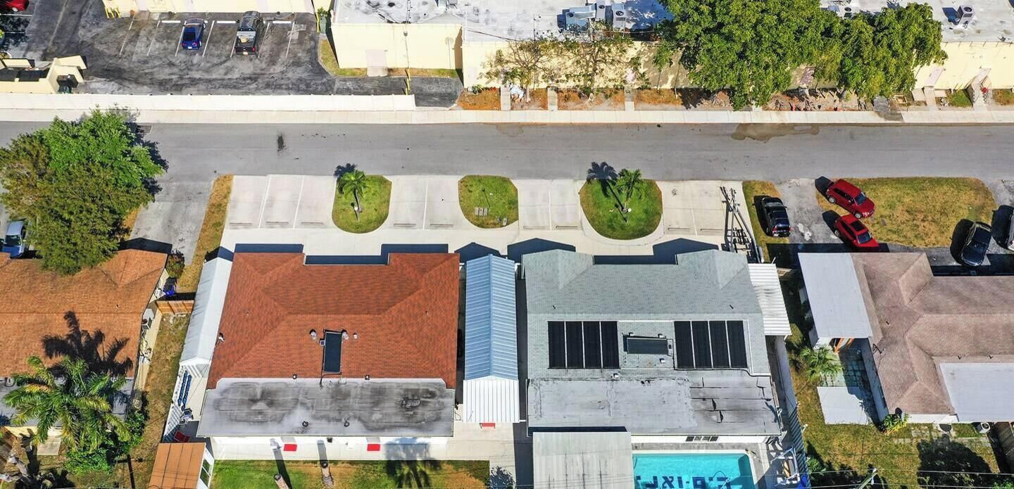 An aerial view of a building with a flat roof, a swimming pool, and a parking lot.