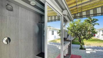 Un baño moderno con ducha, toallero y puerta de vidrio que da a un espacio exterior con un árbol y un camino.
