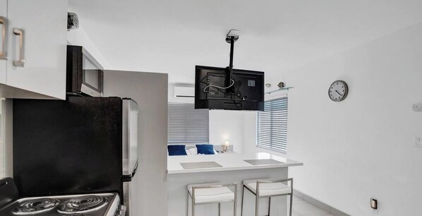 Una cucina compatta con fornello, microonde e un piccolo bancone con due sgabelli.