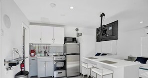 A compact kitchen with white cabinets, a microwave, a stove, and a refrigerator. There is a small bar area with stools. - Studio w/pool & patio, walk to beach (Deerfield Beach)