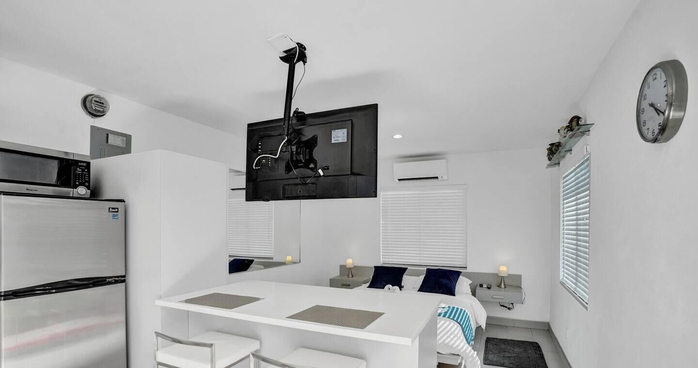 A compact kitchen with a microwave, refrigerator, and a flat-screen TV mounted on the wall.