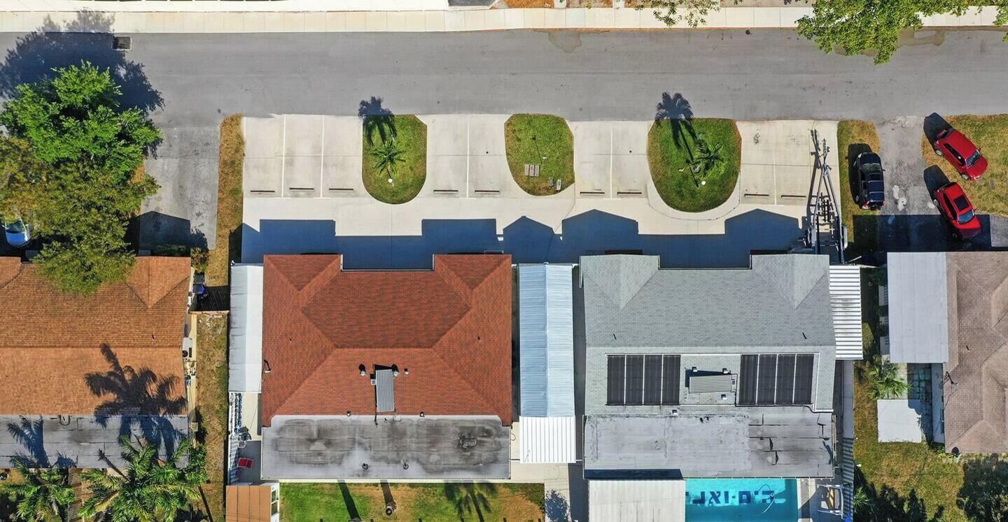 An aerial view of a parking lot with multiple cars, a building with a red roof, and green landscaped areas.