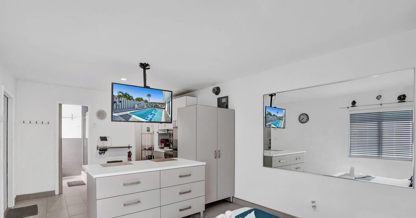 Un bagno moderno con uno specchio grande, una televisione sopra il lavabo e un mobile bagno bianco.