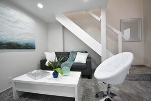 Ein modernes Wohnzimmer mit einem weißen Sofa, einem weißen Sessel, einem Couchtisch mit Dekoration und einer Treppe.