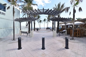 A covered outdoor seating area with benches, palm trees, and a stone wall restaurant. - Loft w/queen bed & steps to Hollywood Beach (Hollywood)