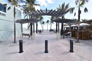 Een overdekt terras met banken, palmbomen en een restaurant met stenen muur.