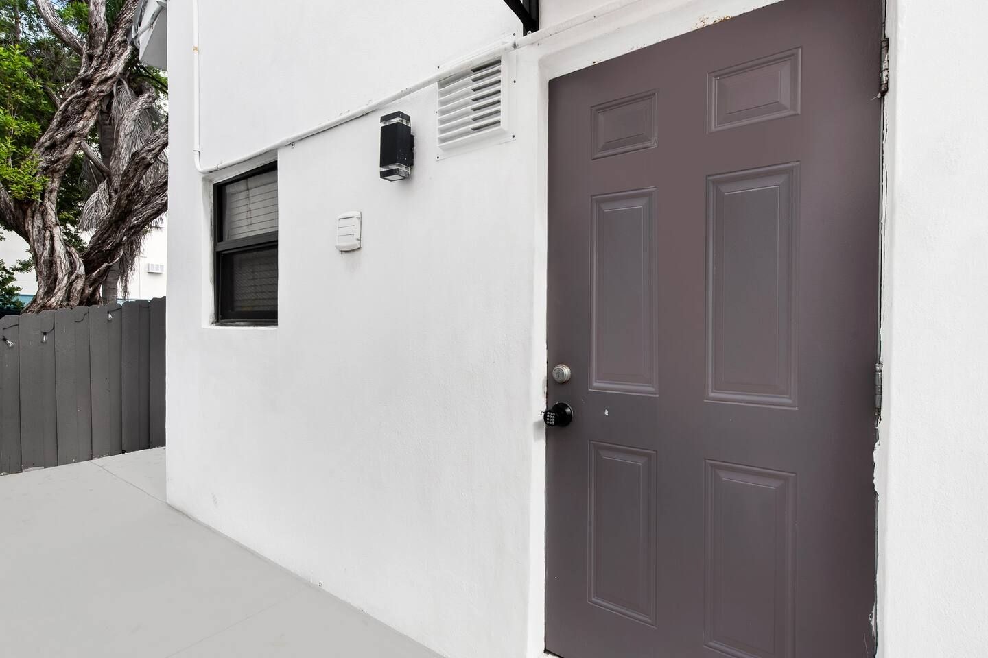 A white building with a brown door, a window, and a small vent.