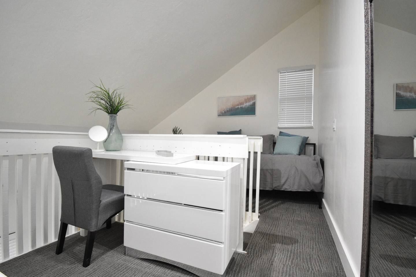 A bedroom with a desk, chair, and a bed with a grey bedspread.