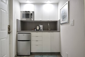 Eine kompakte Küchenzeile mit Mikrowelle, Kaffeemaschine und Kühlschrank.