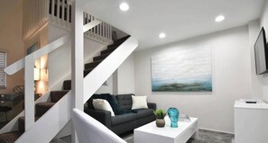Ein modernes Wohnzimmer mit Treppe, einer Couch, einem Couchtisch und einem Gemälde an der Wand.