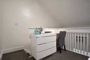 Ein kleines, weißes Schlafzimmer im Loft-Stil mit Schreibtisch und Stuhl, einem Schminktisch und einem Fenster mit Jalousien.