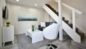 Un salon moderne avec un escalier, un téléviseur à écran plat, une table basse agrémentée d’objets décoratifs et un grand tableau abstrait.