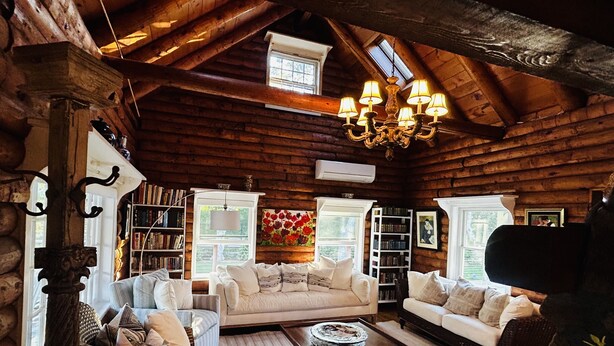 L’intérieur d’un chalet confortable, avec un plafond en bois, un lustre, deux canapés blancs, une table basse et des étagères remplies de livres.