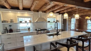 Une cuisine spacieuse dotée d’un grand îlot central, de poutres apparentes en bois et d’appareils électroménagers modernes.