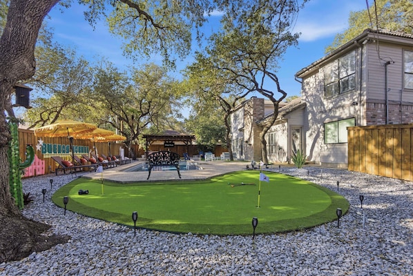 A backyard with a putting green, a wooden bench, and a play area with a slide.