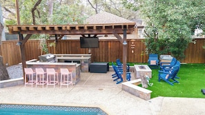 An outdoor patio with a grill, seating, and a TV screen.