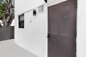 A white building with a brown door, a window, and a small vent. - Loft w/queen loft & beach steps (Hollywood)