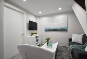 Ein modernes Wohnzimmer mit Flachbildfernseher, einem Gemälde, einer Couch und einem Couchtisch.