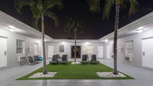 Un cortile con zona salotto, palme e un edificio con porte e finestre.