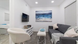 Un soggiorno moderno con un divano grigio, una poltrona bianca, un tavolino da caffè e un quadro raffigurante una spiaggia.