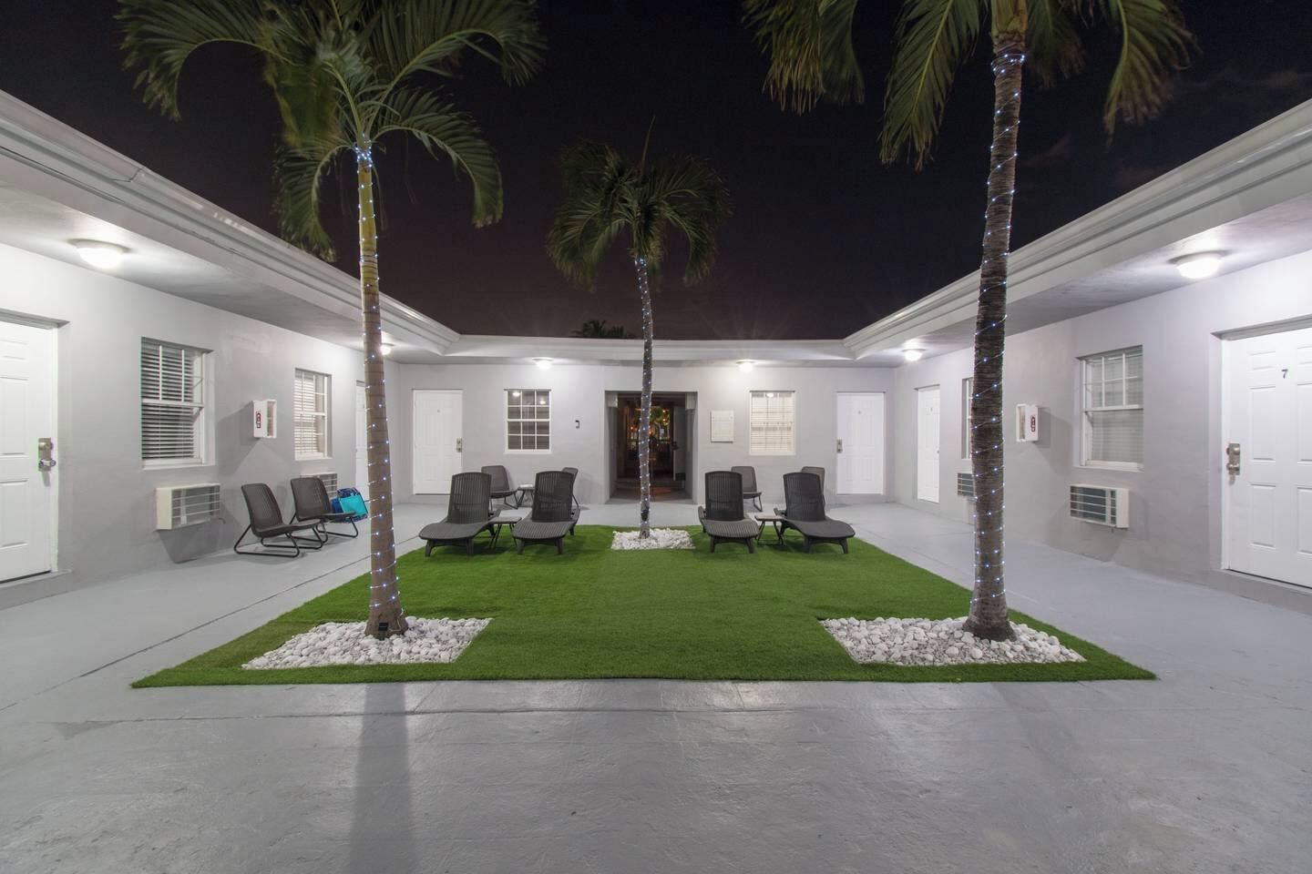 A courtyard with a seating area, palm trees, and a building with doors and windows.