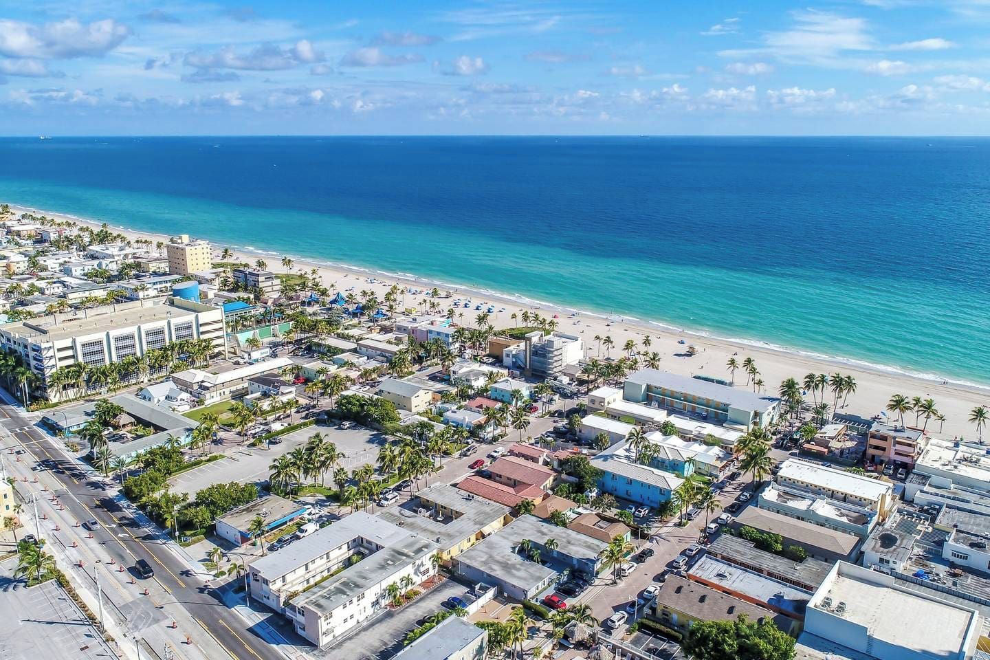 Vista aérea de un pueblo costero con playa, edificios y un cielo azul despejado.