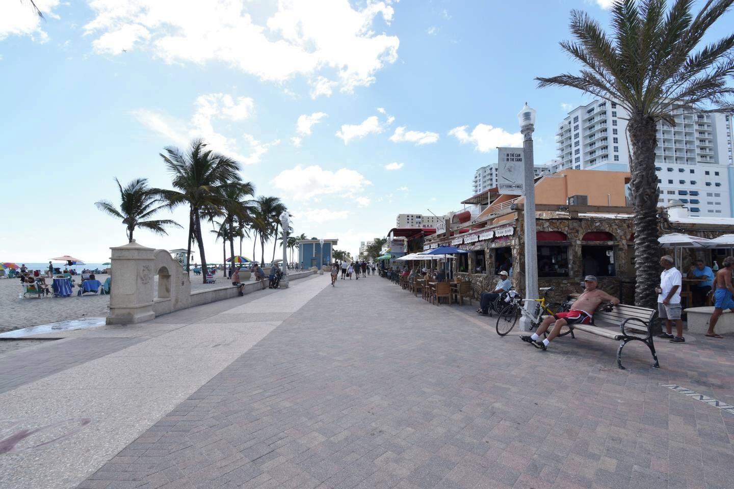 Une promenade en bord de mer bordée de palmiers, avec des terrasses et une rangée de restaurants.