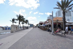 Une promenade en bord de mer bordée de palmiers, avec des terrasses et une rangée de restaurants.