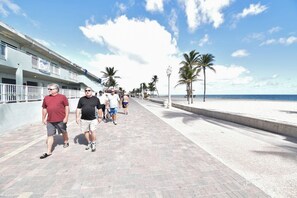 A paved walkway with a beach and palm trees on the right, and a building with a sign on the left. - Modern studio w/queen bed & beach views (Hollywood)