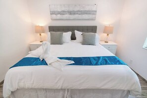 Ein ordentlich bezogenes Bett mit blauem Akzent, zwei Nachttischlampen und einem grauen Kopfteil.