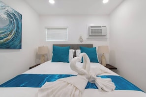 Une chambre d’hôtel avec un lit, deux tables de chevet, une fenêtre avec des stores, un appareil de climatisation et un tableau au mur.
